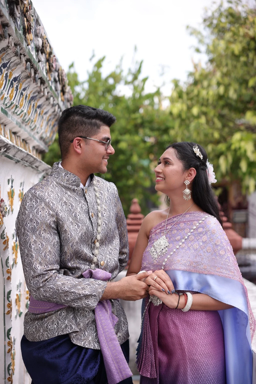 Malika and Jyanesh holding hands beside a decorated temple wall